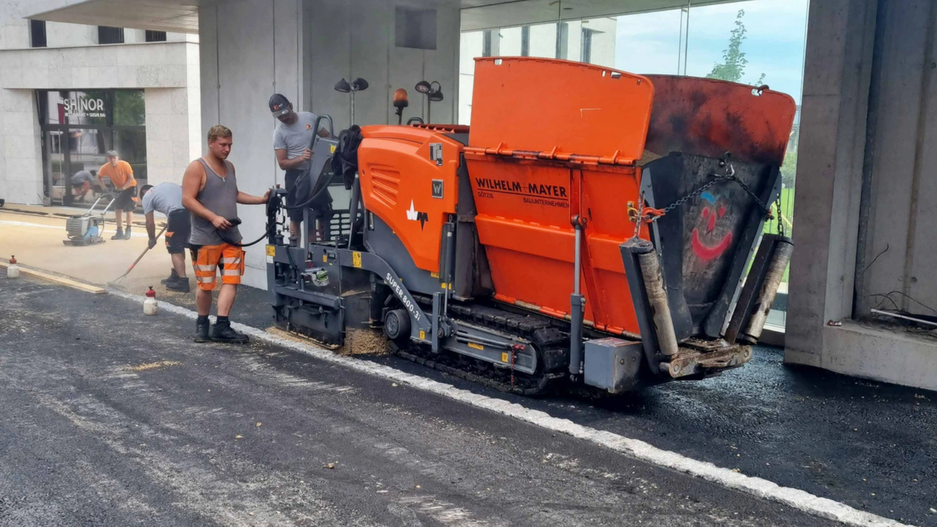 Fertiger und Arbeiter vor Gebäude bei Asphaltierarbeiten von Wilhelm+Mayer Bau am Garnmart in Götzis.