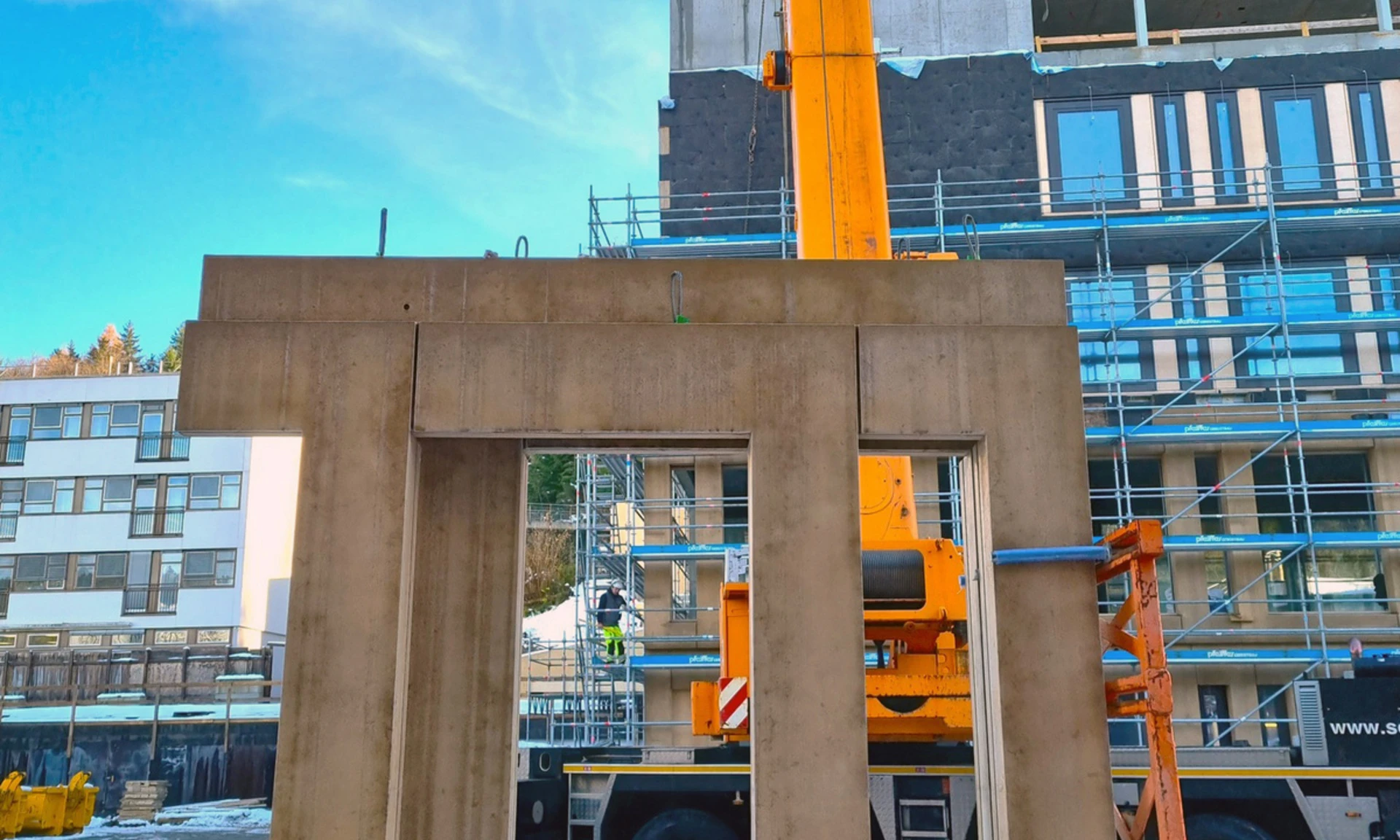 Ein Fassadenelement aus Beton steht zum Einbau mittels Mobilkran und Monteuren vor dem Neubau des LKH Rankweil bereit.